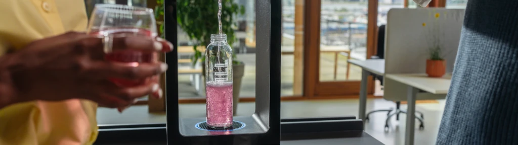 Two people using Aquablu touchscreen water dispenser to fill a bottle with flavoured water